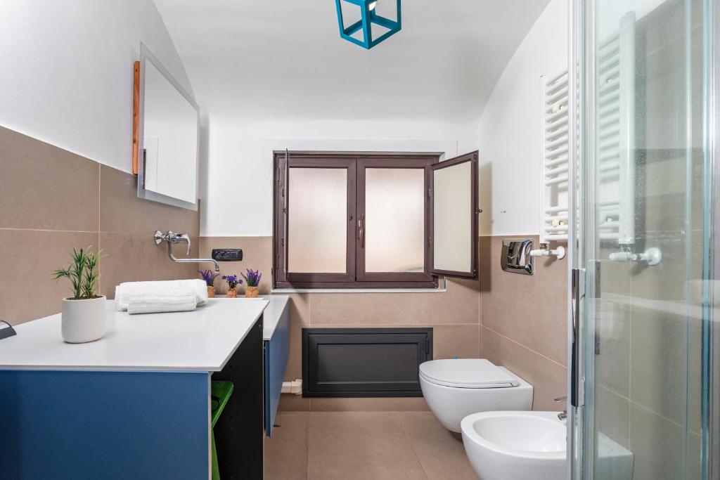 Bagno con mobile lavabo blu, finestra, sanitari e box doccia in vetro